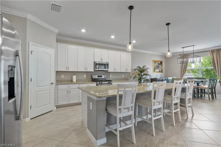 Kitchen featuring a kitchen island with sink, white cabinetry, hanging light fixtures, stainless steel appliances, and light tile patterned floors