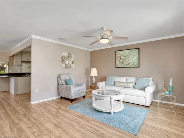 Living area featuring light wood-style flooring, baseboards, ceiling fan, and crown molding