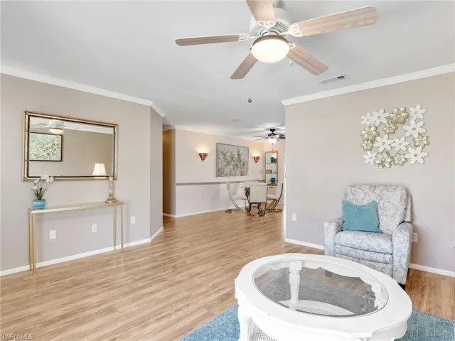 Living area with ornamental molding, light wood-style flooring, baseboards, and a ceiling fan