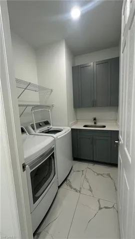 Laundry area featuring cabinet space, light marble finish floors, and washer and dryer