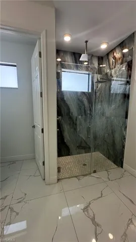 Bathroom featuring light marble finish floors and a marble finish shower
