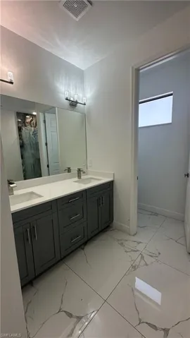 Full bath with double vanity, a stall shower, and light marble finish flooring