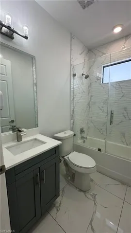 Full bath with enclosed tub / shower combo, vanity, and light marble finish floors