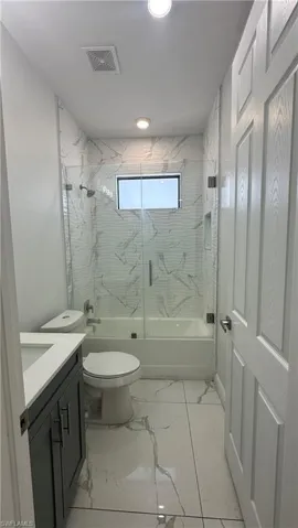 Full bath with enclosed tub / shower combo, vanity, and light marble finish floors