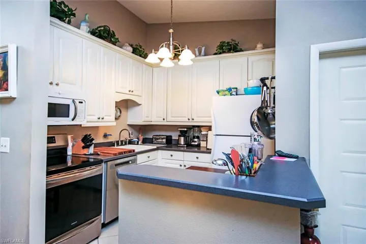 Kitchen with stainless steel appliances, sink, kitchen peninsula, white cabinetry, and a notable chandelier