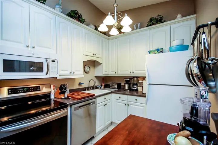 Kitchen with white cabinetry, light tile patterned floors, an inviting chandelier, appliances with stainless steel finishes, and sink