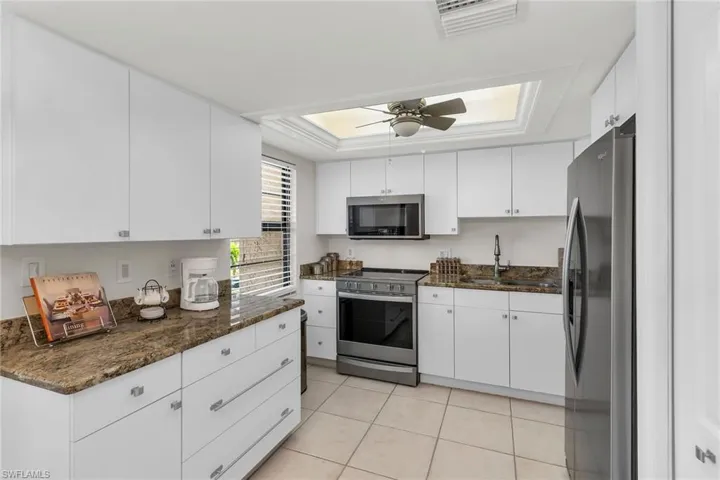 Kitchen with appliances with stainless steel finishes, dark stone countertops, white cabinets, and a tray ceiling