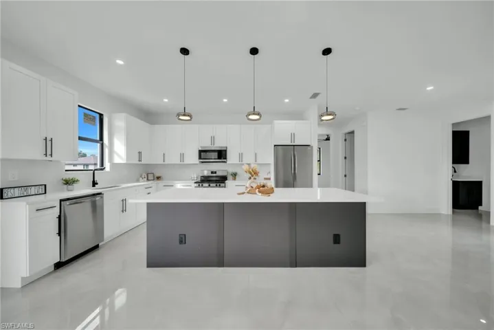 Dual tone kitchen featuring a center island, decorative light fixtures, stainless steel appliances, light stone countertops, and two tone cabinets