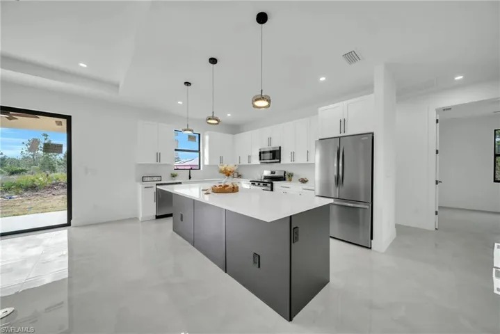 Kitchen featuring stainless steel appliances, two tone cabinetry, a center island, hanging light fixtures, and light stone counters