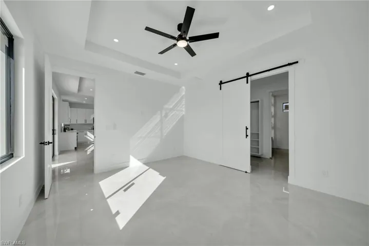 Unfurnished living room featuring recessed lighting, a barn door, a ceiling fan, and a raised ceiling