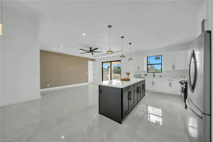 Kitchen with pendant lighting, stainless steel appliances, two tone cabinetry, open floor plan, and light stone countertops
