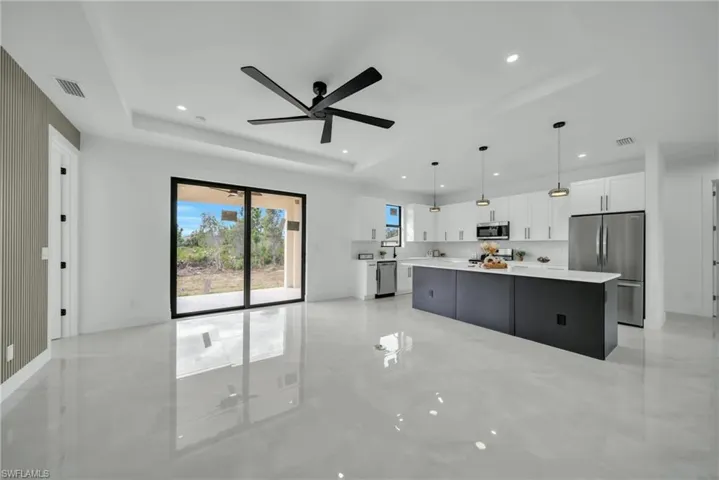 Two tone kitchen featuring a ceiling fan, stainless steel appliances, decorative light fixtures, a tray ceiling, and a center island