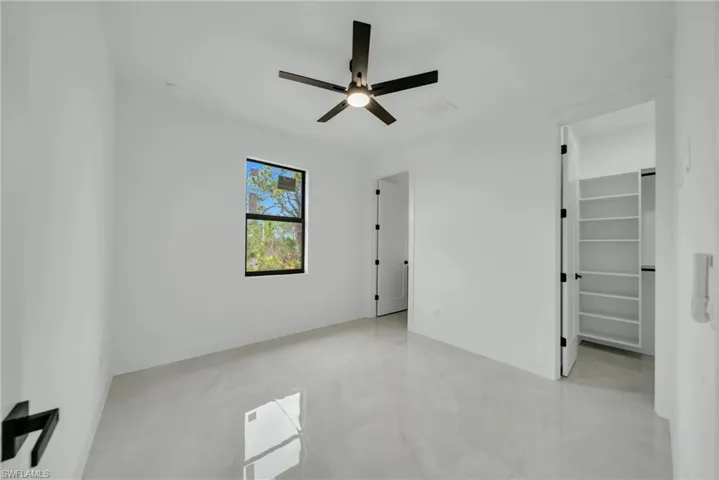 Unfurnished bedroom with a walk in closet, a ceiling fan, and finished concrete flooring