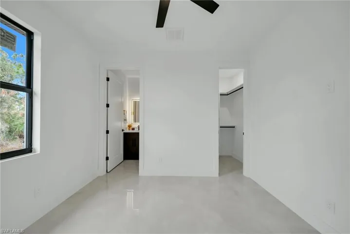 Unfurnished bedroom featuring a walk in closet, ceiling fan, and ensuite bath