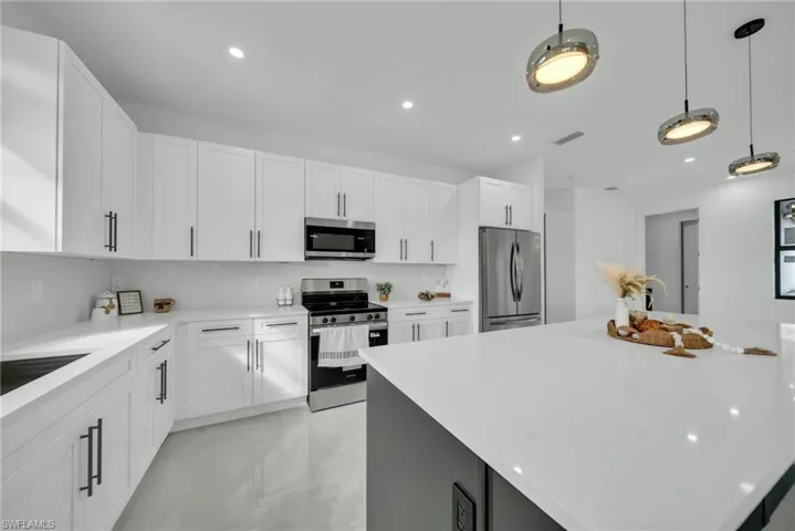 Dual tone kitchen featuring stainless steel appliances, pendant lighting, a center island, light stone countertops, and dual tone cabinetry