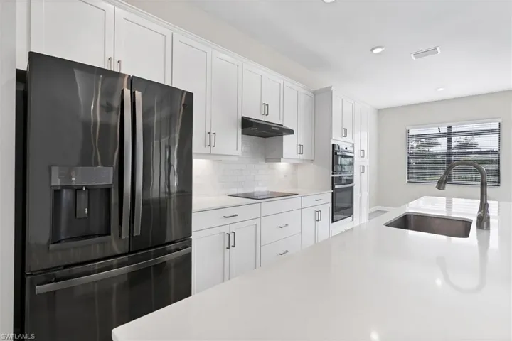 Kitchen with black appliances, light countertops, under cabinet range hood, white cabinets, and decorative backsplash