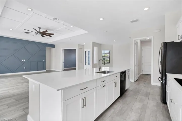 Kitchen featuring a ceiling fan, a kitchen island with sink, black appliances, light countertops, and recessed lighting
