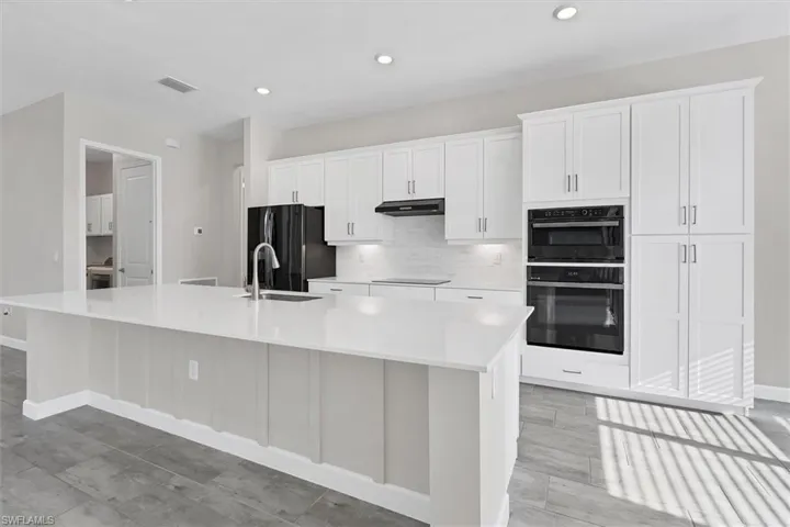 Kitchen with black appliances, a large island, under cabinet range hood, white cabinetry, and light countertops