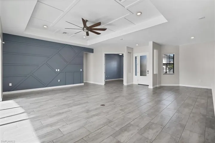Unfurnished living room featuring a raised ceiling, a ceiling fan, recessed lighting, and a decorative wall