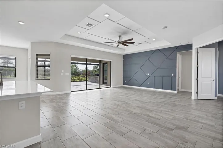 Unfurnished living room featuring a raised ceiling, ceiling fan, an accent wall, and recessed lighting