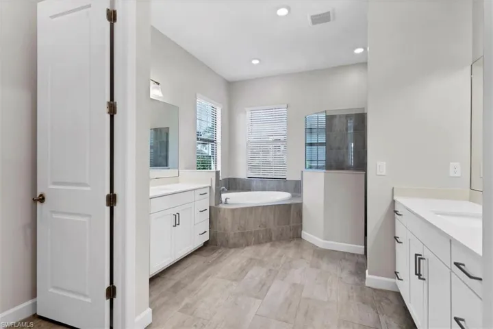 Full bathroom with two vanities, a bath, and recessed lighting