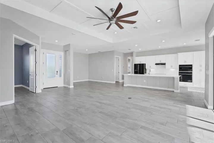Unfurnished living room with a ceiling fan, a tray ceiling, and recessed lighting