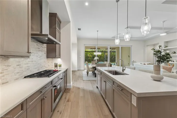 Kitchen with light hardwood / wood-style flooring, stainless steel appliances, backsplash, wall chimney exhaust hood, and sink