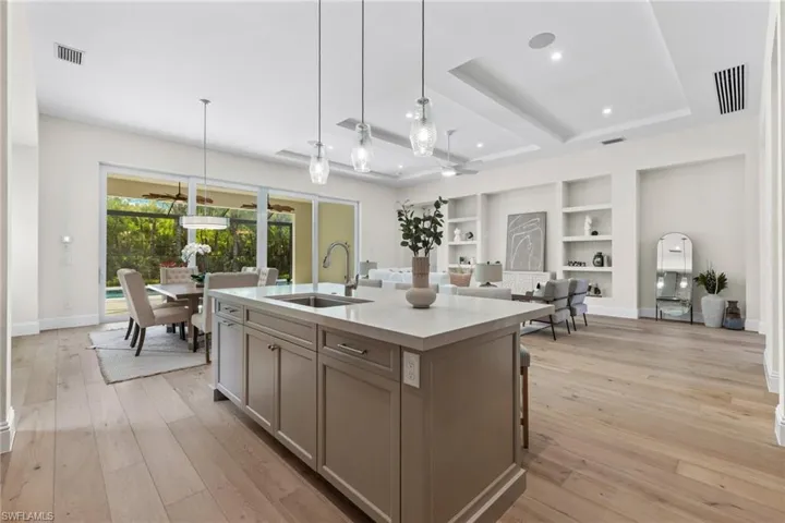 Kitchen featuring a tray ceiling, a kitchen island with sink,  touchless faucet, light wood-type flooring, sink, and pendant lighting
