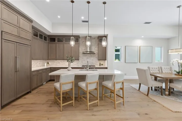 Kitchen featuring tasteful backsplash, an island with sink, light wood-type flooring, pendant lighting, and wall chimney range hood