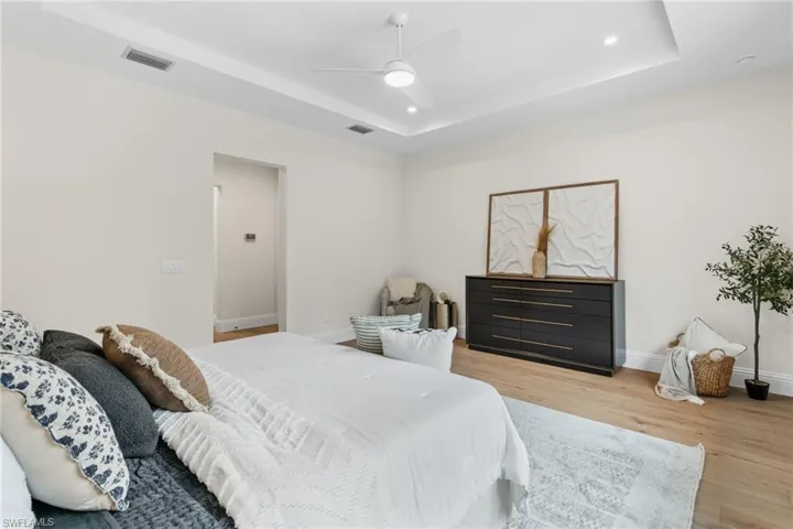 Bedroom with light hardwood / wood-style floors, ceiling fan, and a raised ceiling