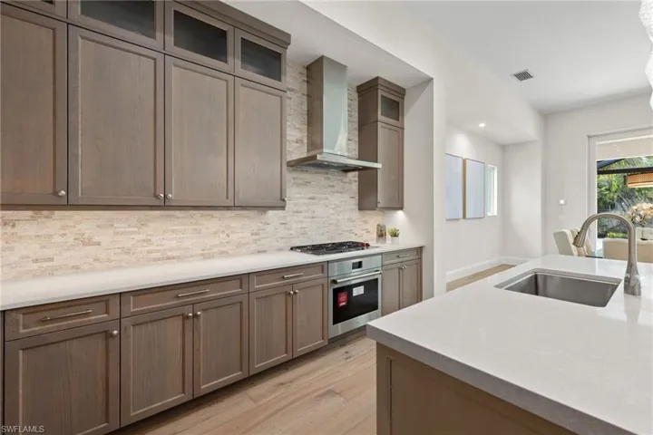 Kitchen featuring wall chimney range hood, light wood-type flooring, appliances with stainless steel finishes, sink, and tasteful backsplash