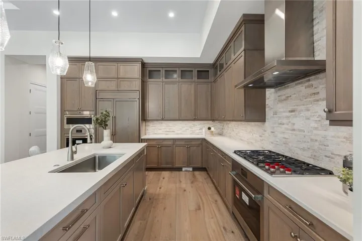 Kitchen featuring light hardwood / wood-style flooring, backsplash, hanging light fixtures, wall chimney exhaust hood, and appliances with stainless steel finishes