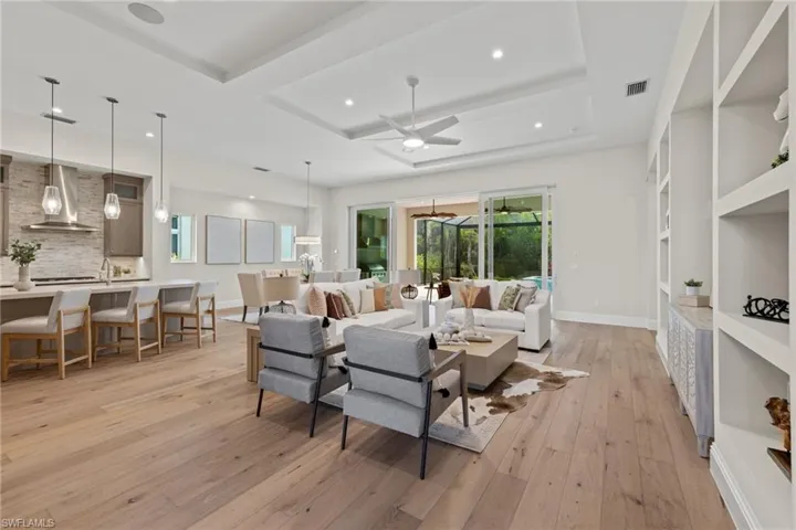 Living room with a tray ceiling, built in shelves, light wood-type flooring, and ceiling fan