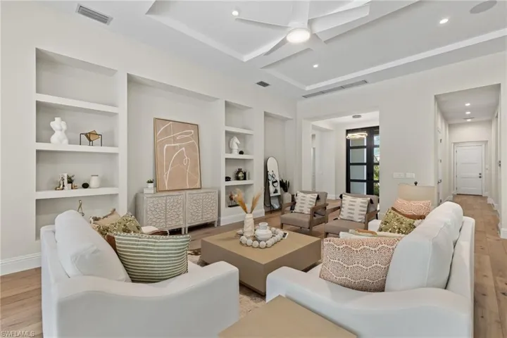 Living room with built in shelves, light wood-type flooring, and ceiling fan