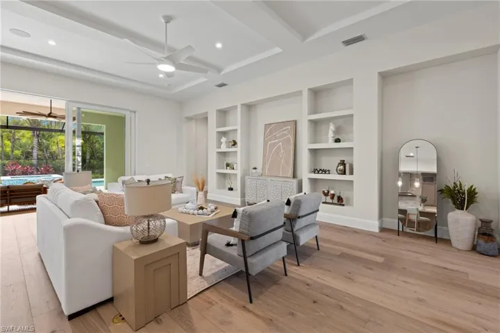 Living room with beam ceiling, built in features, ceiling fan, and light hardwood / wood-style flooring
