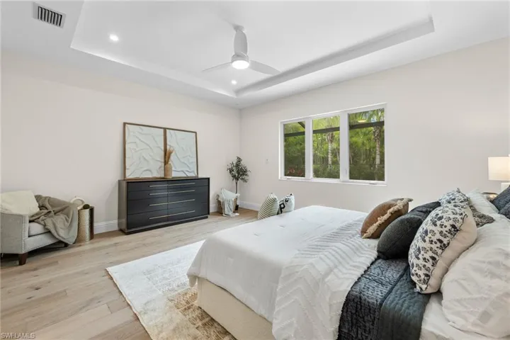 Bedroom with light wood-type flooring, ceiling fan, and a raised ceiling