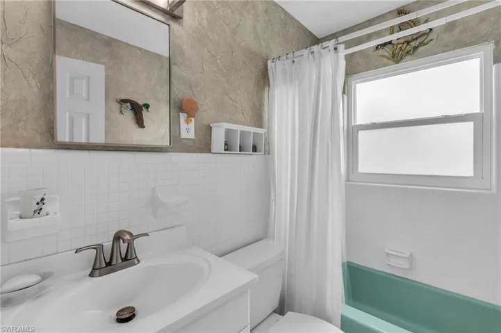 Full bathroom with tile walls, shower / bathtub combination with curtain, toilet, and vanity