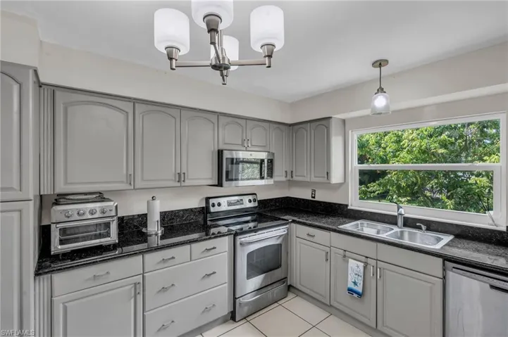 Kitchen with pendant lighting, light tile patterned floors, sink, gray cabinetry, and appliances with stainless steel finishes