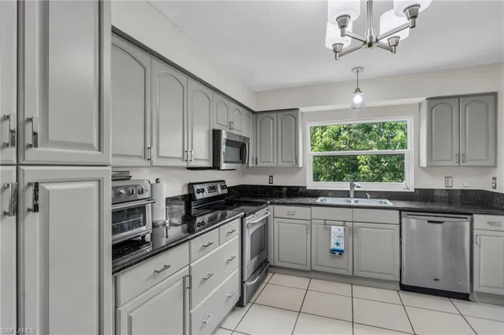 Kitchen with light tile patterned flooring, hanging light fixtures, sink, stainless steel appliances, and an inviting chandelier