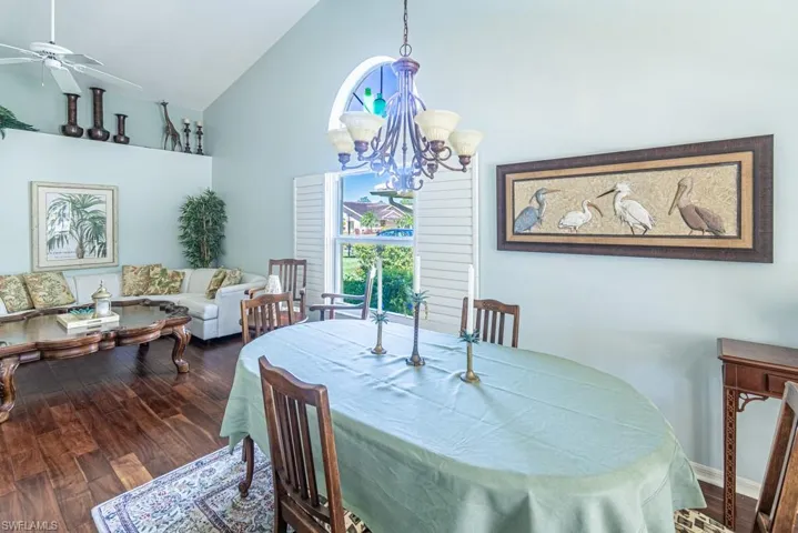 Dining room featuring high vaulted ceiling, wood finished floors, and ceiling fan with notable chandelier
