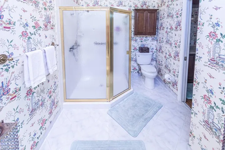 Bathroom featuring wallpapered walls, toilet, and a shower stall