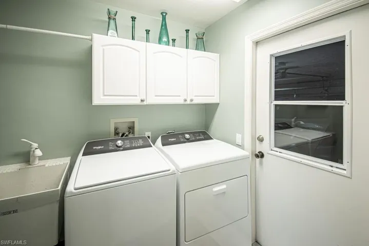 Clothes washing area featuring washing machine and clothes dryer, cabinet space, and a sink