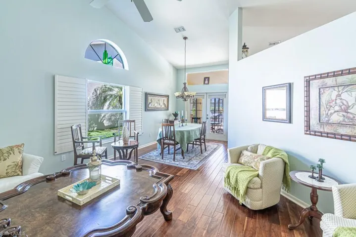 Living room featuring high vaulted ceiling, wood finished floors, baseboards, ceiling fan with notable chandelier, and visible vents