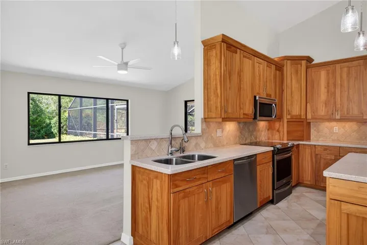 Kitchen with vaulted ceiling, stainless steel appliances, wood finish cabinetry, a ceiling fan, and light stone counters