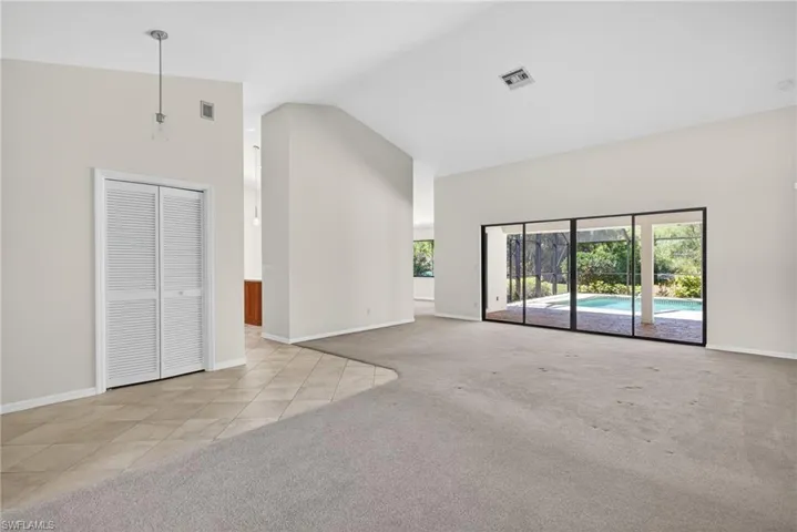 Unfurnished living room featuring light carpet, lofted ceiling, and light tile patterned flooring