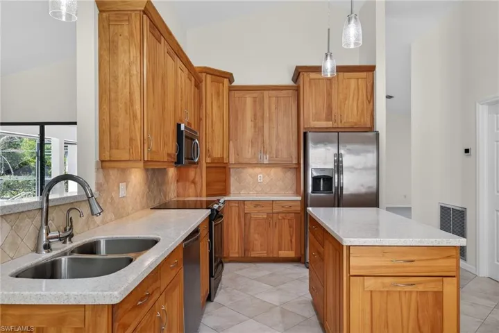 Kitchen with tasteful backsplash, pendant lighting, wood finish cabinetry, stainless steel appliances, and lofted ceiling