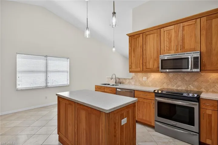 Kitchen with stainless steel appliances, light tile patterned flooring, wood finish cabinets, a center island, and lofted ceiling