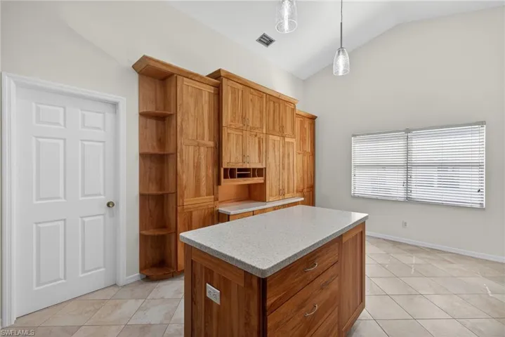 Kitchen featuring a kitchen island, light tile patterned flooring, wood finish cabinetry, lofted ceiling, and open shelves