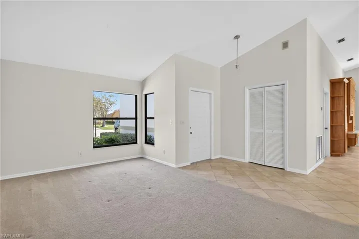 Unfurnished bedroom with lofted ceiling, light colored carpet, a closet, and light tile patterned floors