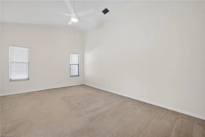 Empty room featuring vaulted ceiling, ceiling fan, and carpet flooring